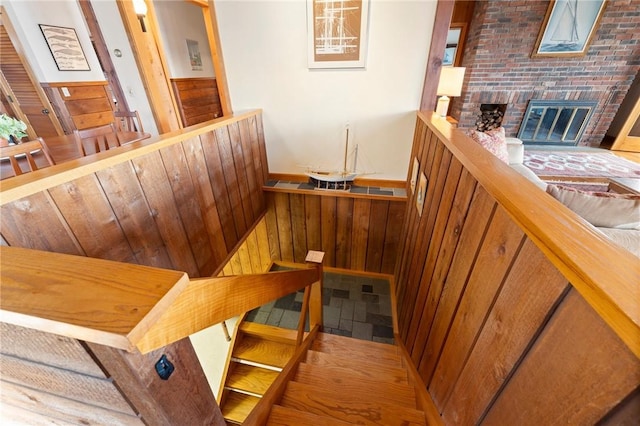 stairway featuring wood walls, a fireplace, and wainscoting
