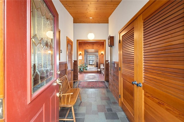 corridor with stone finish flooring, wooden walls, wainscoting, and wood ceiling