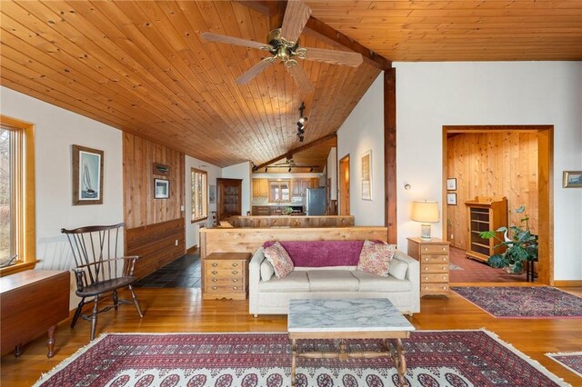 living area with vaulted ceiling, a ceiling fan, wood walls, wood ceiling, and wood finished floors