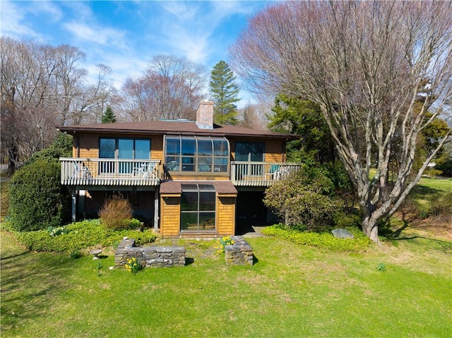 back of house with a sunroom, a chimney, a wooden deck, and a lawn