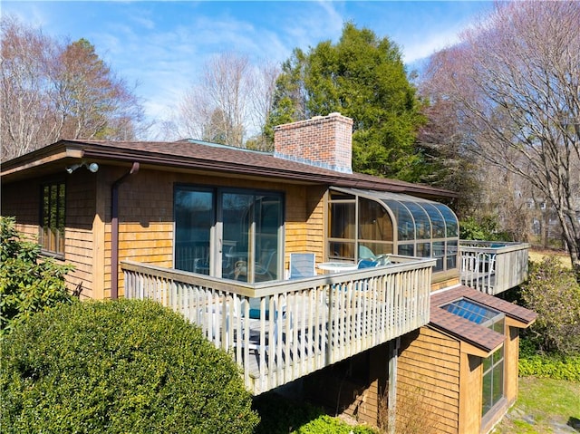 rear view of house with a deck, a sunroom, and a chimney