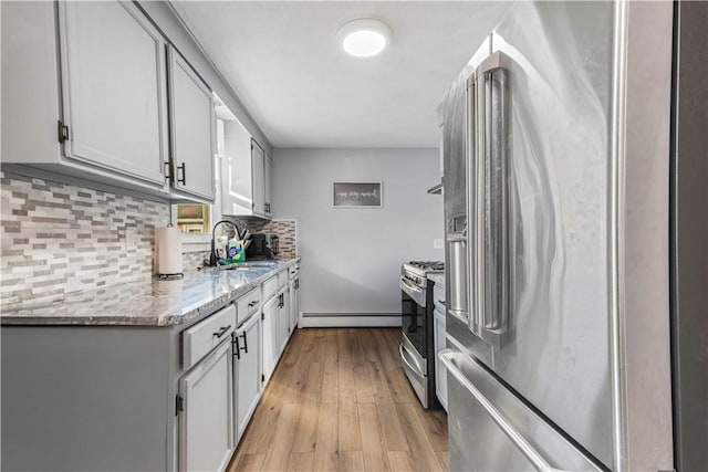 kitchen with a baseboard heating unit, light wood-style flooring, backsplash, stainless steel appliances, and a sink