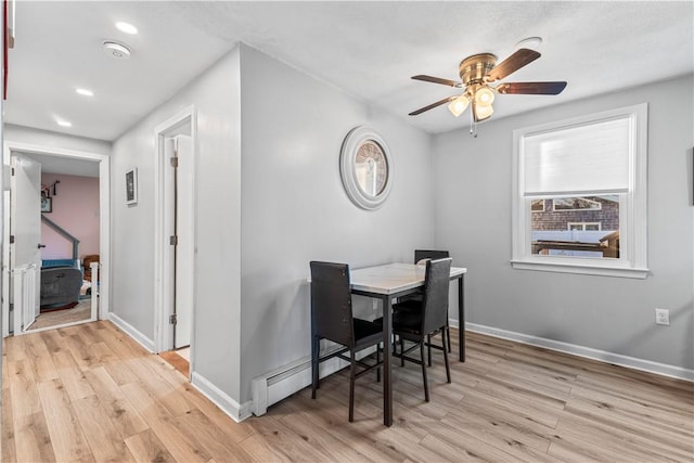 dining space featuring a baseboard radiator, light wood-style flooring, baseboards, and a ceiling fan