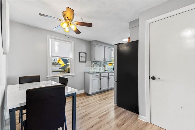 kitchen featuring freestanding refrigerator, tasteful backsplash, a ceiling fan, light wood finished floors, and baseboards