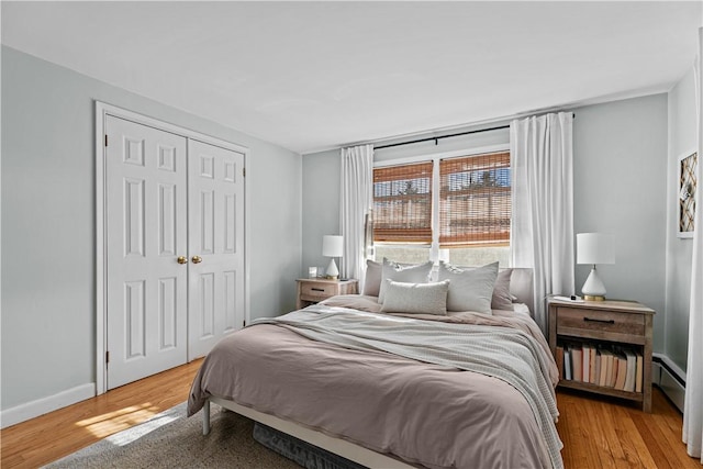 bedroom with a closet, light wood-style flooring, a baseboard radiator, and baseboards