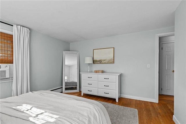 bedroom with cooling unit, wood finished floors, a baseboard heating unit, and baseboards