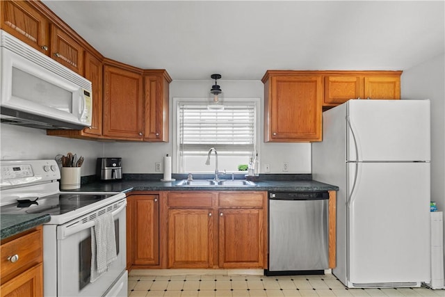 kitchen featuring white appliances, dark countertops, brown cabinets, light floors, and a sink