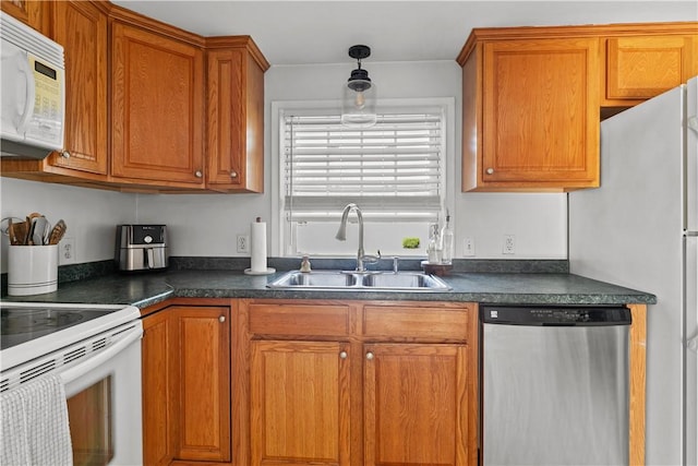 kitchen with pendant lighting, white appliances, a sink, dark countertops, and brown cabinets