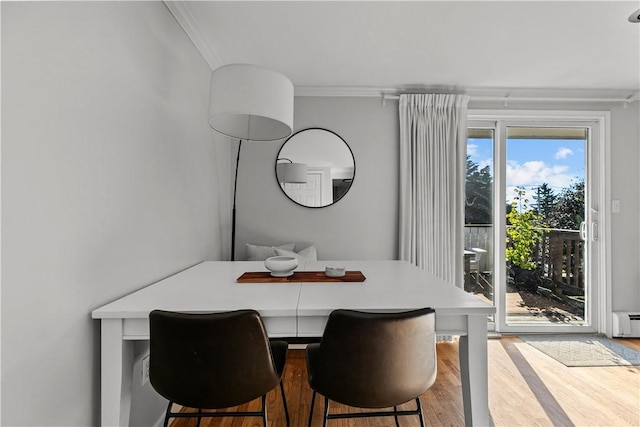 dining space with ornamental molding, a baseboard radiator, and wood finished floors