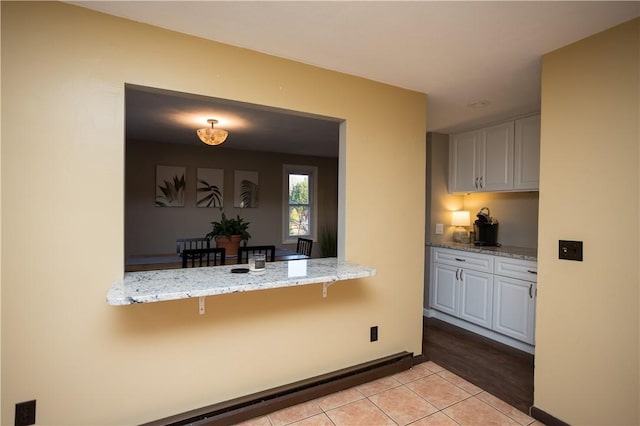 67 Highwood Dr, Coventry, RI 02816 - kitchen featuring a baseboard radiator, a kitchen breakfast bar, baseboards, light stone countertops, and light tile patterned flooring