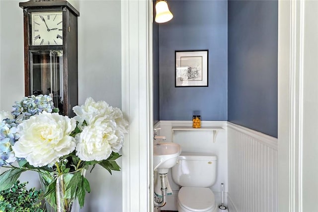 half bath with a decorative wall, toilet, and wainscoting