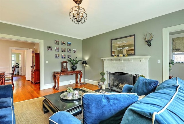 living room with a notable chandelier, a brick fireplace, baseboards, and wood finished floors