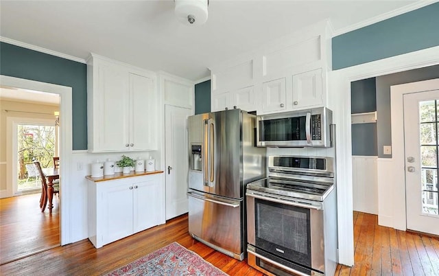 kitchen featuring stainless steel appliances, white cabinets, hardwood / wood-style flooring, and crown molding