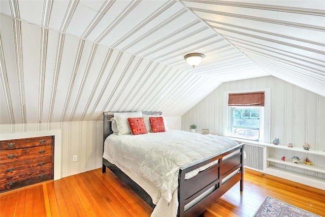 bedroom with wood finished floors, radiator heating unit, and vaulted ceiling