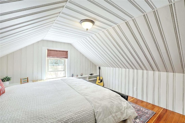 bedroom with wood finished floors, wallpapered walls, and lofted ceiling