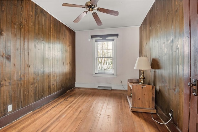 unfurnished room featuring ceiling fan, visible vents, wood walls, baseboards, and hardwood / wood-style floors