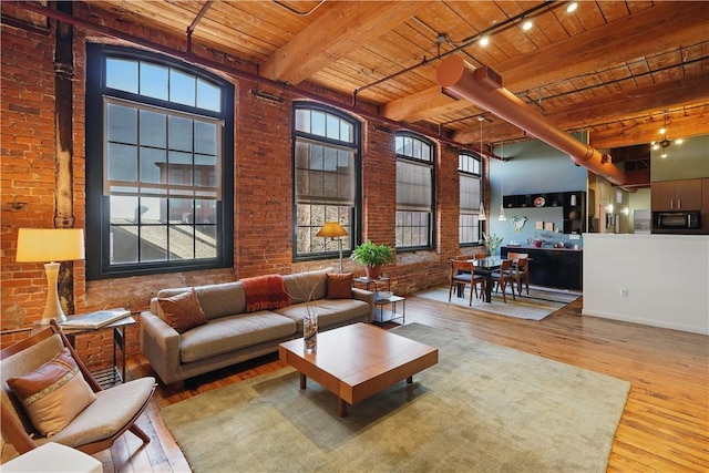 living room with beamed ceiling, rail lighting, wood ceiling, brick wall, and wood-type flooring