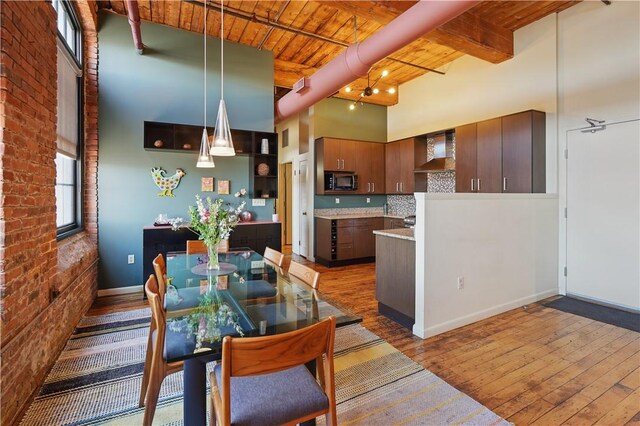 dining space featuring baseboards, brick wall, beam ceiling, wood-type flooring, and wood ceiling