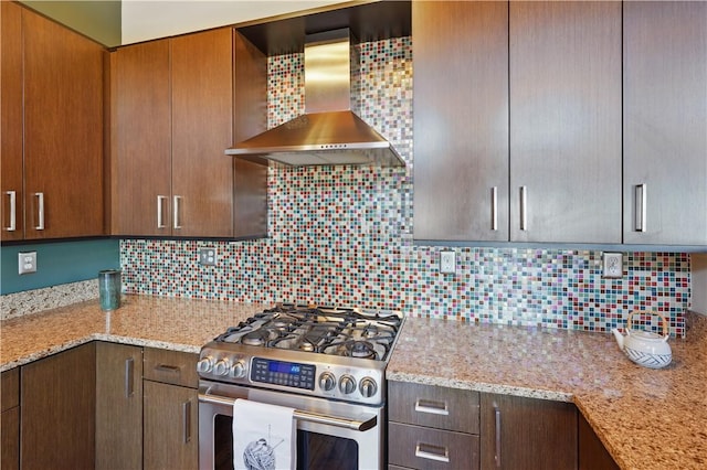 kitchen featuring decorative backsplash, gas stove, wall chimney exhaust hood, and light stone counters