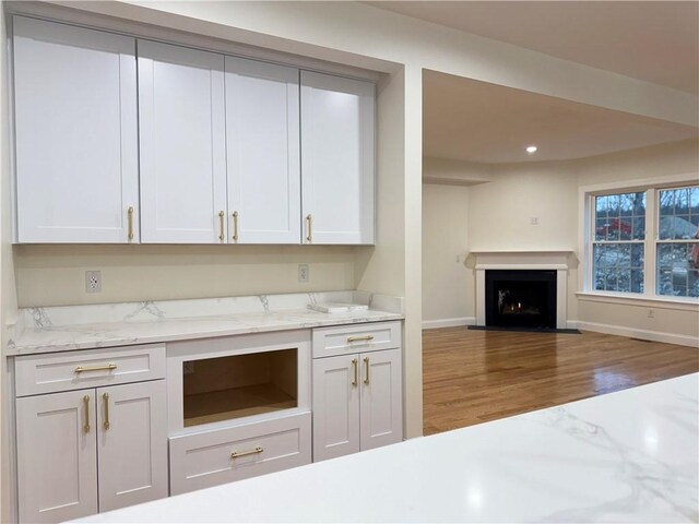 1404 Hunting Hill Dr, Cumberland, RI 02864 - kitchen featuring open floor plan, baseboards, wood finished floors, a warm lit fireplace, and light stone counters