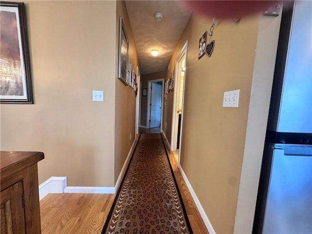 hall featuring an upstairs landing, baseboards, and light wood-style floors