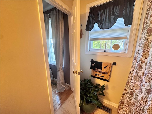 corridor featuring baseboards, visible vents, and wood finished floors