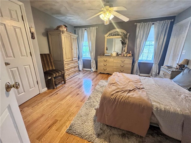 bedroom featuring a ceiling fan, multiple windows, light wood-style flooring, and baseboards