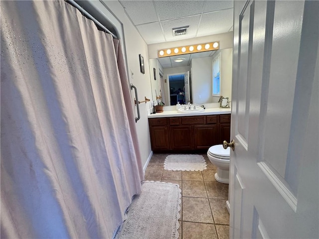 full bath with tile patterned floors, toilet, double vanity, visible vents, and a drop ceiling