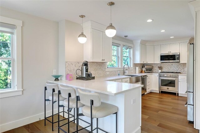 137 Rosebriar Ave, South Kingstown, RI 02879 - kitchen with a peninsula, white cabinetry, wood finished floors, stainless steel appliances, and decorative backsplash
