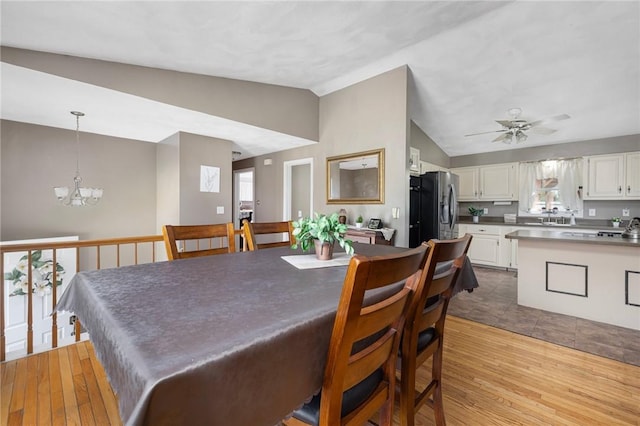 dining space featuring light wood finished floors, lofted ceiling, and ceiling fan with notable chandelier