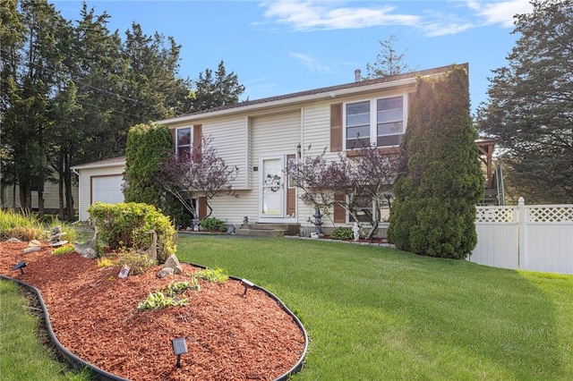 bi-level home with entry steps, a front lawn, fence, and a garage