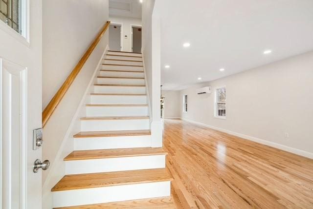 staircase featuring wood finished floors, a wall mounted air conditioner, baseboards, and recessed lighting