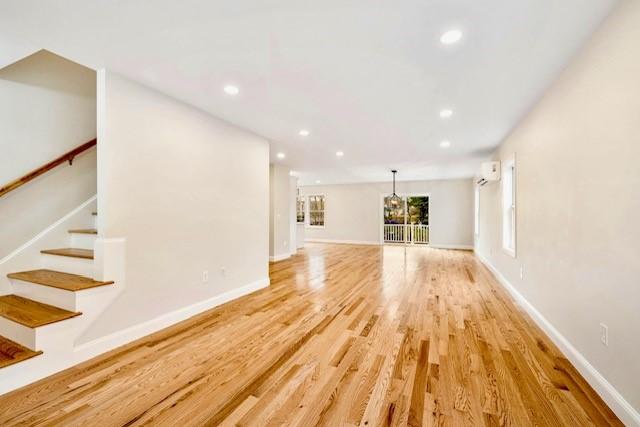 unfurnished living room with stairway, baseboards, recessed lighting, and light wood-style floors