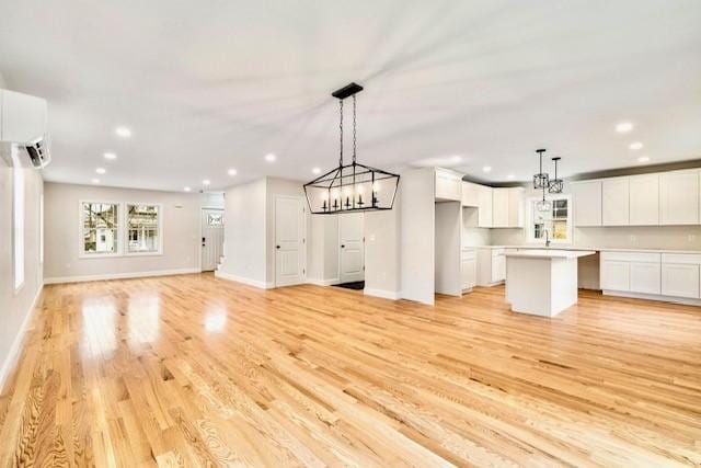 unfurnished living room with baseboards, an inviting chandelier, recessed lighting, light wood-style flooring, and a wall unit AC