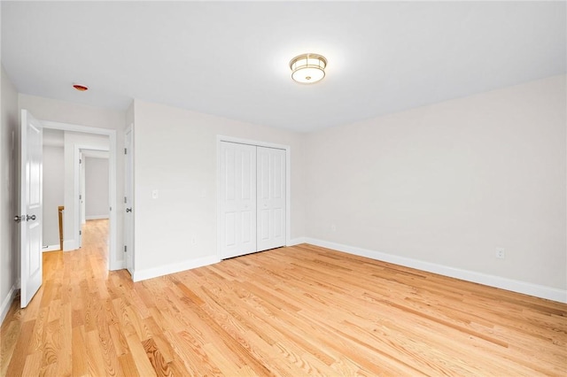 unfurnished bedroom with light wood-style flooring, a closet, and baseboards