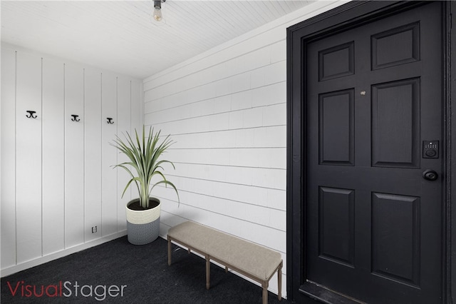 mudroom featuring dark carpet, wooden walls, and baseboards