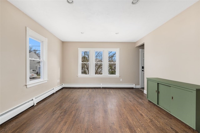 spare room featuring baseboard heating, dark wood-style flooring, baseboards, and a wealth of natural light