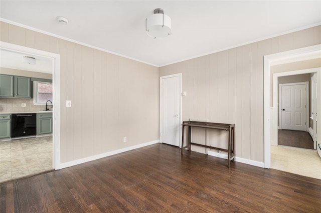 spare room with baseboards, a sink, ornamental molding, and wood finished floors