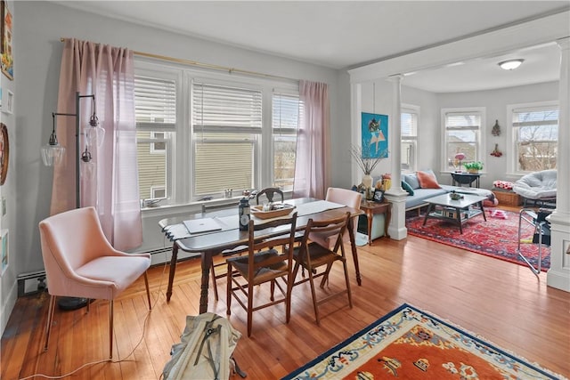 dining area featuring ornate columns, wood finished floors, and baseboard heating