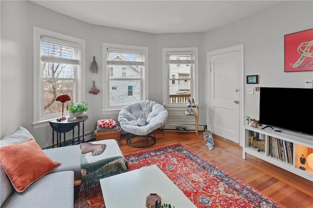 living area with a baseboard radiator, a healthy amount of sunlight, and wood finished floors
