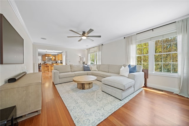 living area with ornamental molding, ceiling fan, and wood finished floors