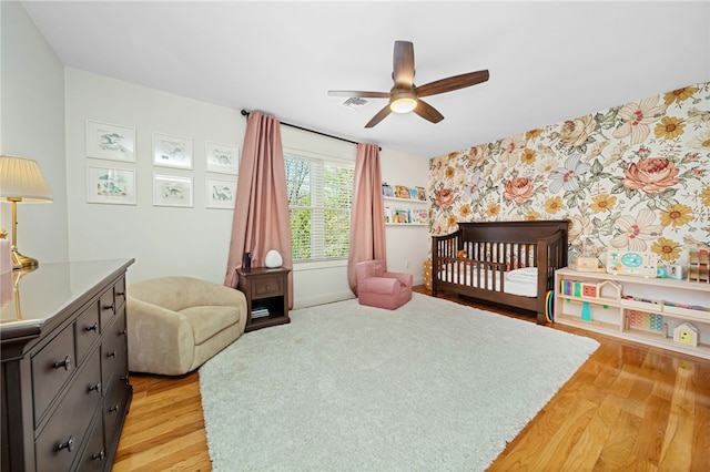 bedroom featuring a crib, an accent wall, light wood finished floors, and wallpapered walls