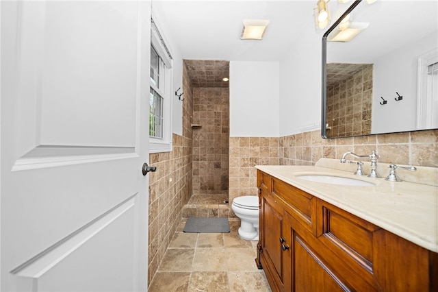 full bath featuring stone finish floor, tile walls, a tile shower, vanity, and toilet
