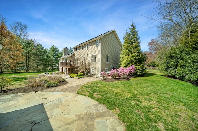 exterior space with a deck, a patio, a chimney, a lawn, and stairway