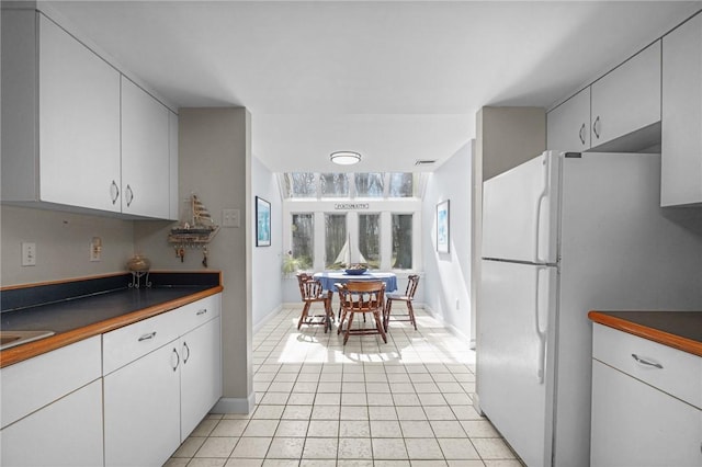 kitchen featuring white cabinets, dark countertops, freestanding refrigerator, and light tile patterned flooring