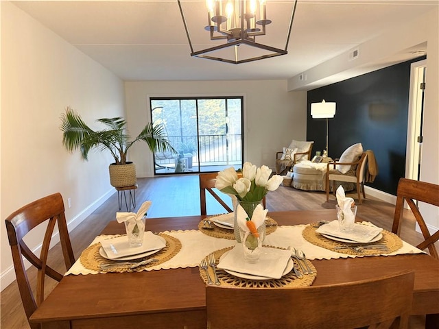 dining area featuring wood finished floors, visible vents, a notable chandelier, and baseboards