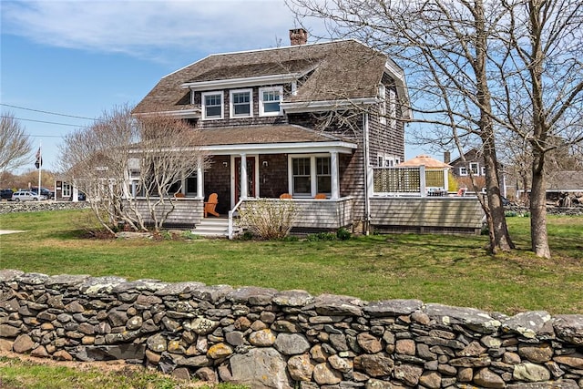 shingle-style home with a front yard, covered porch, and a chimney