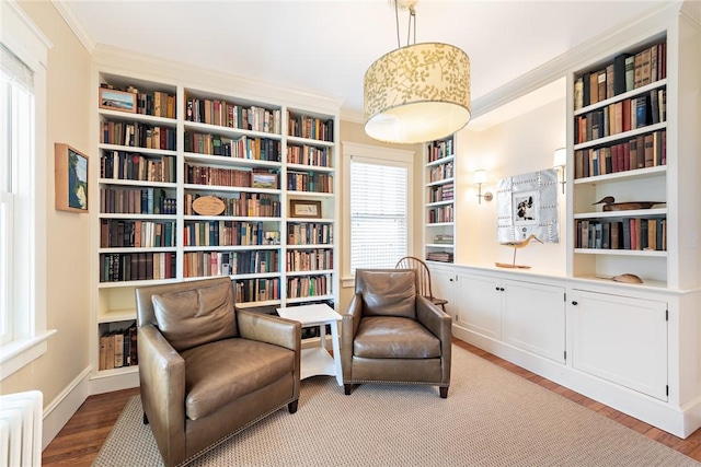 sitting room featuring light wood-style floors, crown molding, and wall of books