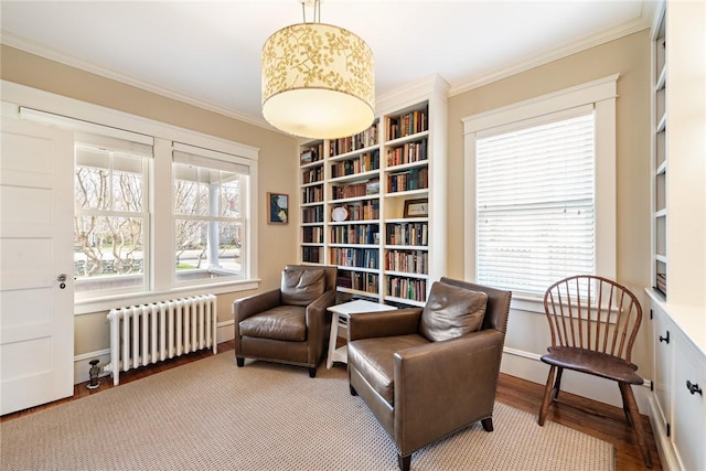 living area featuring radiator, built in features, crown molding, baseboards, and wood finished floors