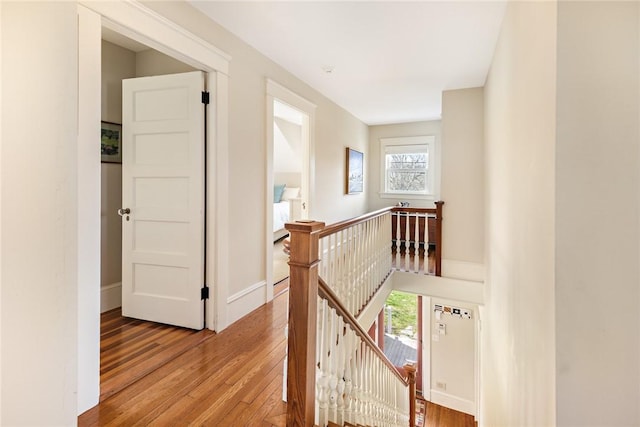 hall with an upstairs landing, hardwood / wood-style floors, and baseboards